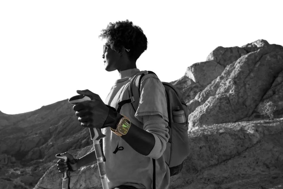 A person hiking in the mountains with poles and a backpack, wearing Apple Watch Ultra